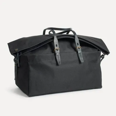 A black canvas weekender bag with leather handles by Bleu de Chauffe.